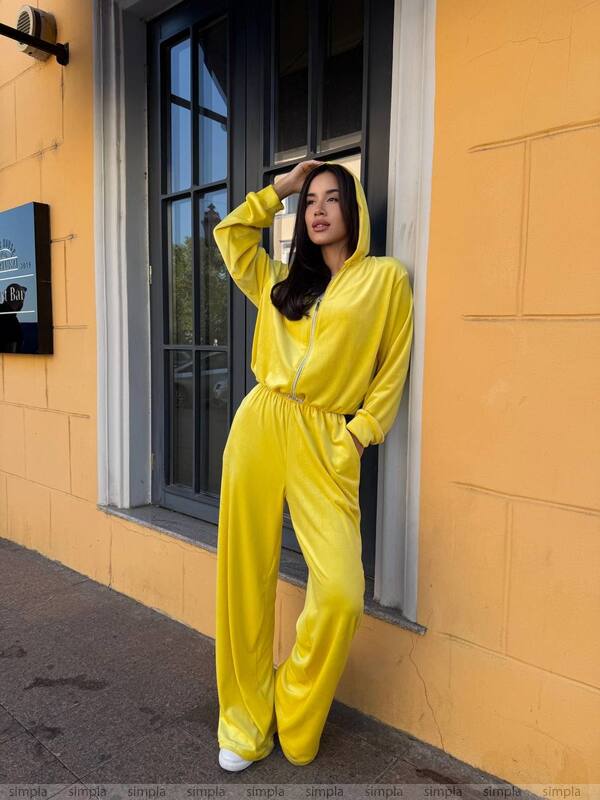 Person wearing a yellow tracksuit standing against a yellow wall.