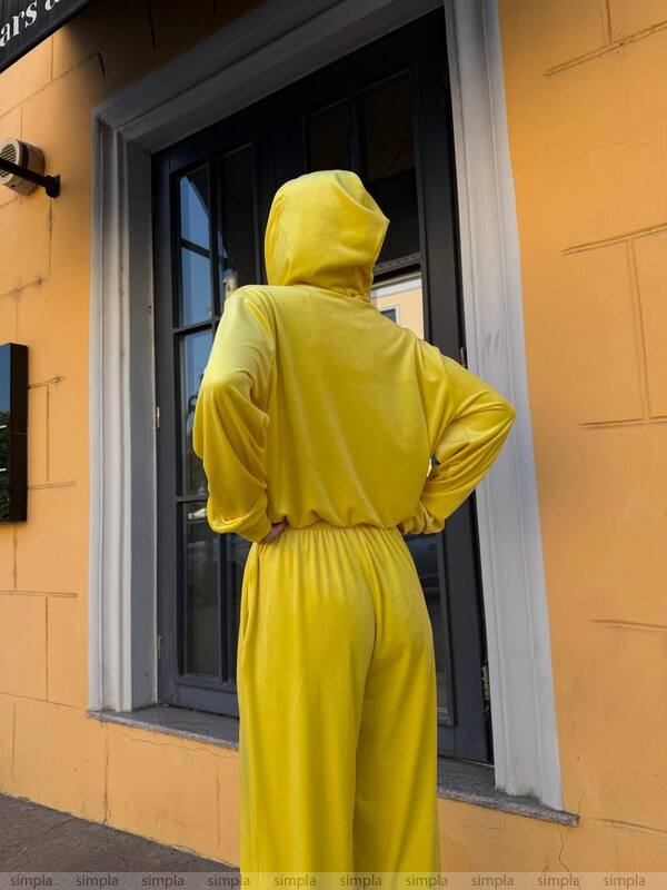 Person wearing a yellow tracksuit standing in front of a yellow building.