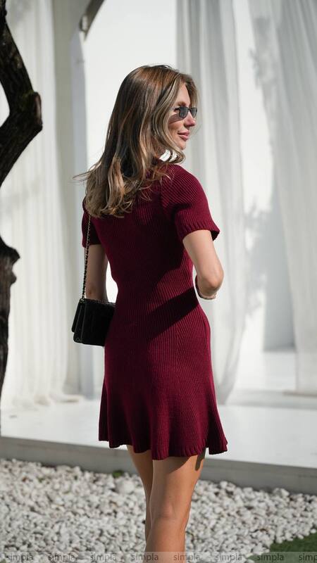 Woman wearing a burgundy dress with a black belt in front of classical columns.