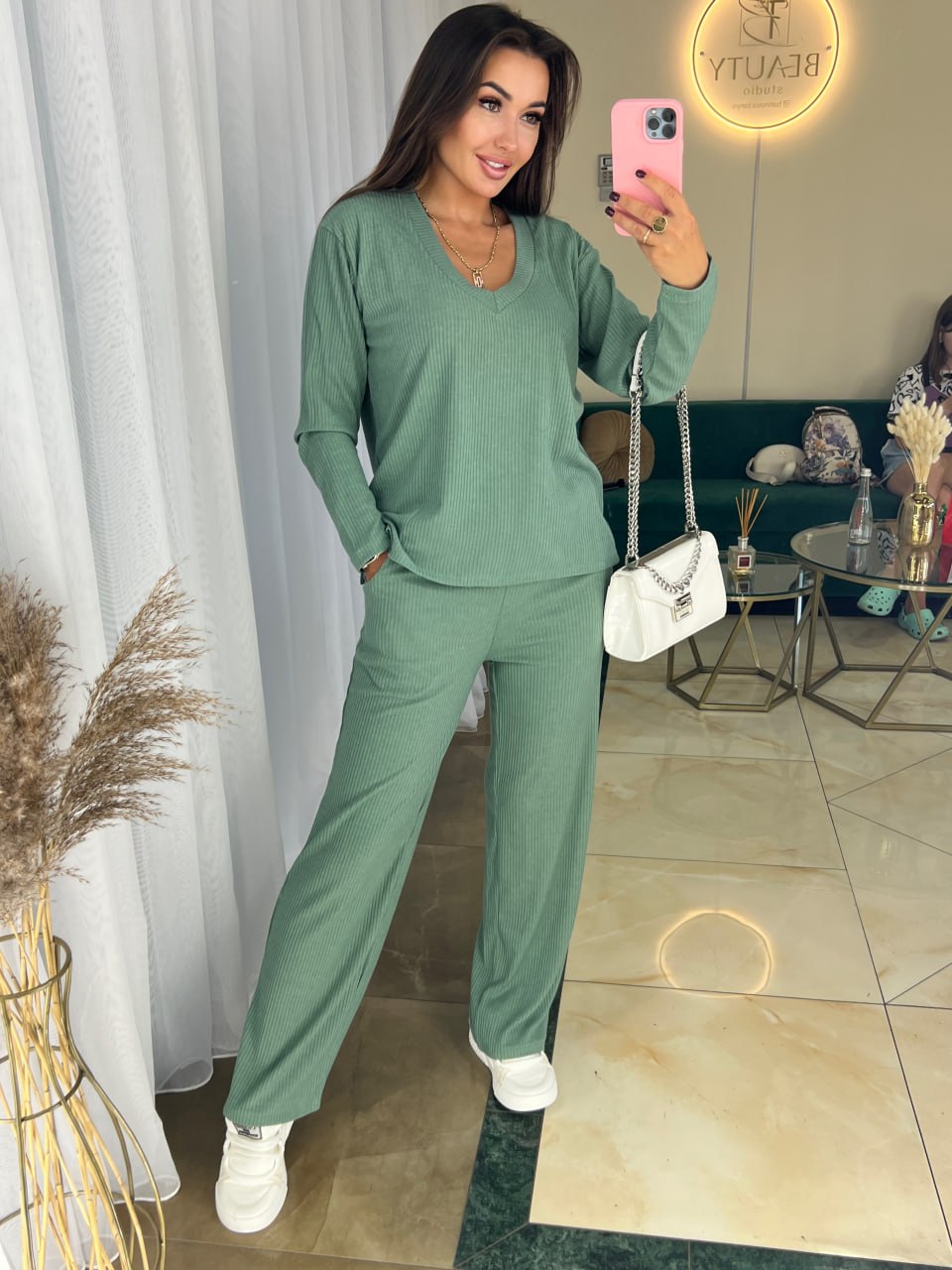 Woman in a green outfit taking a mirror selfie in a living room.