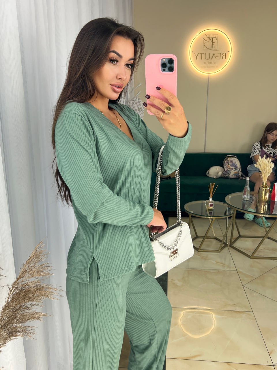 Woman in a green outfit taking a mirror selfie in a stylish room.