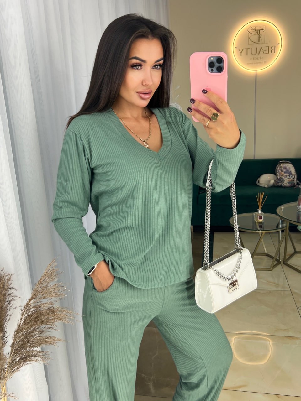 Woman in a green outfit taking a selfie in a room with decor elements.