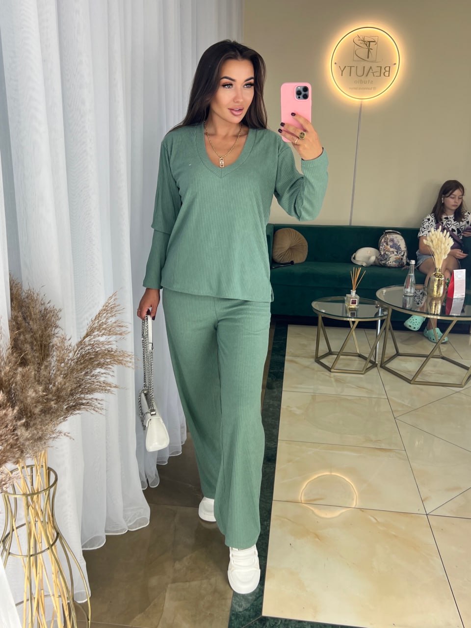 Woman taking a mirror selfie wearing a green outfit in a modern living room.