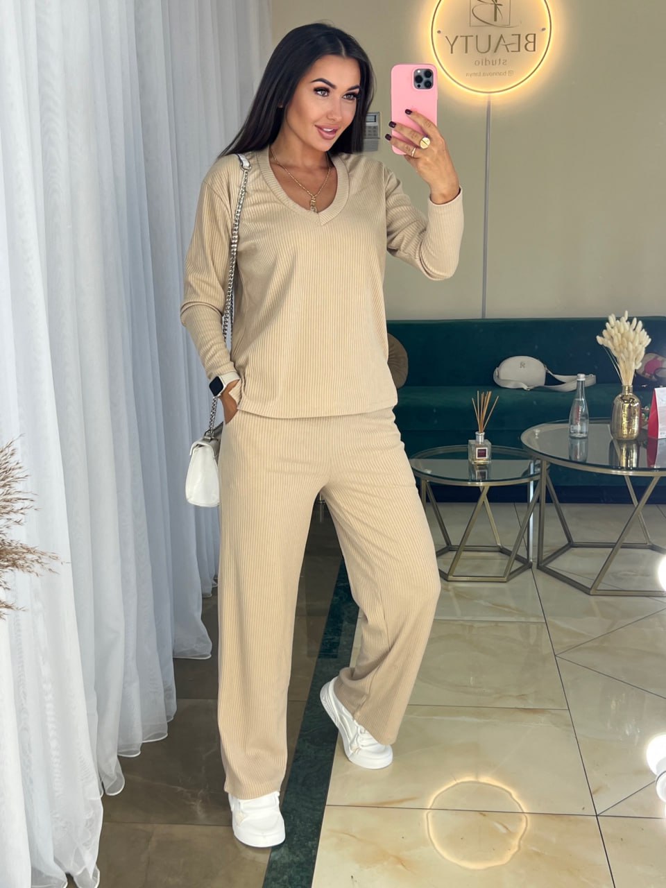Woman in beige outfit taking a mirror selfie in a modern living room.