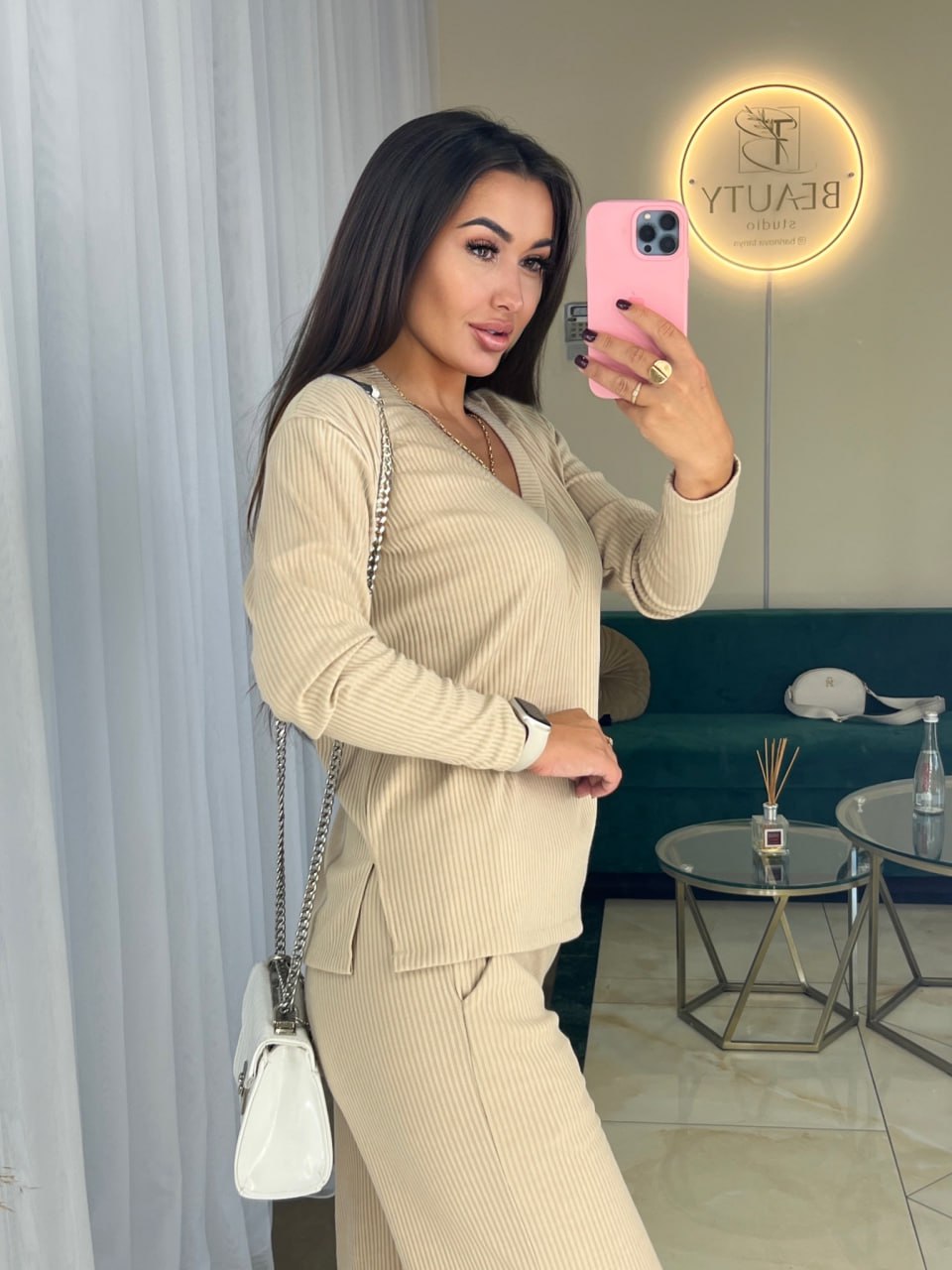 Woman taking a mirror selfie in a beige outfit with a blurred background