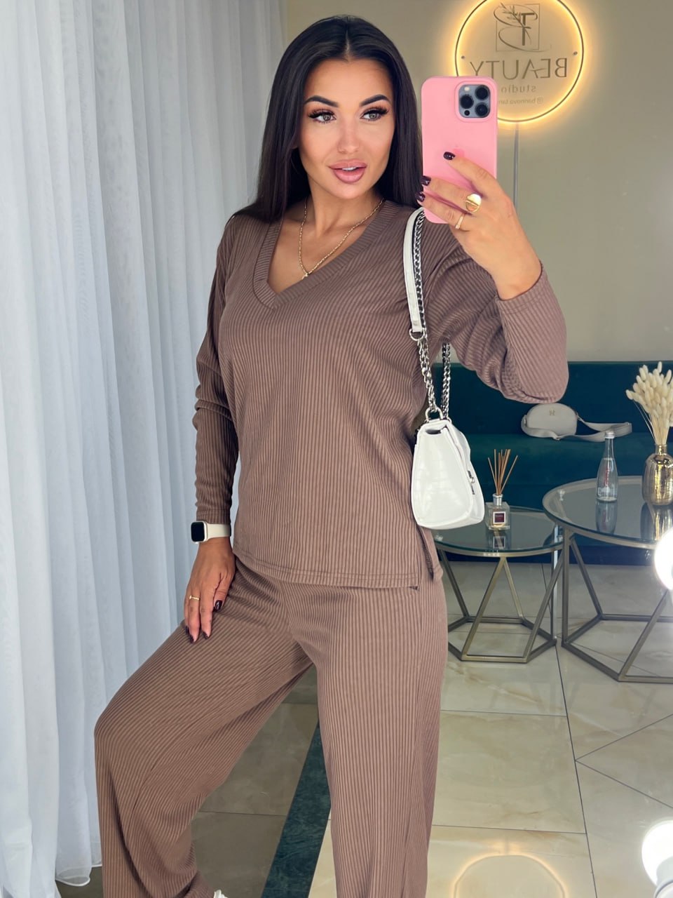 Woman taking a mirror selfie wearing a brown ribbed outfit in a modern interior setting.