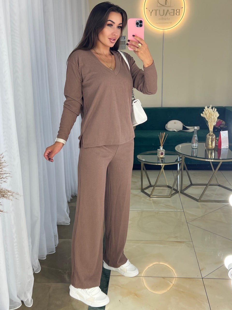 Woman taking a mirror selfie wearing a brown outfit in a living room.