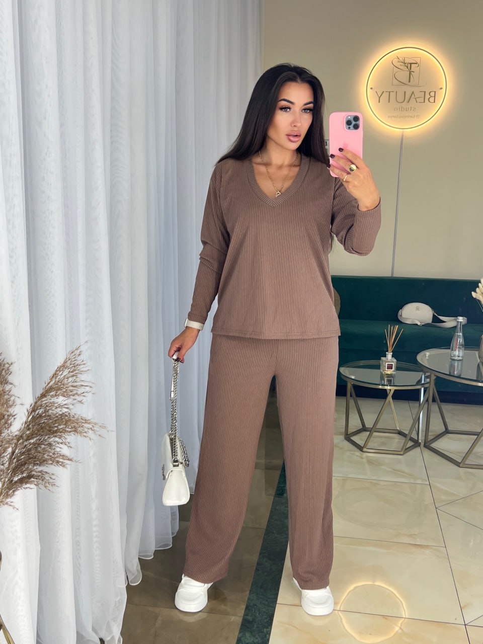 Woman taking a mirror selfie wearing a brown outfit in a room with a green sofa and decorative items.