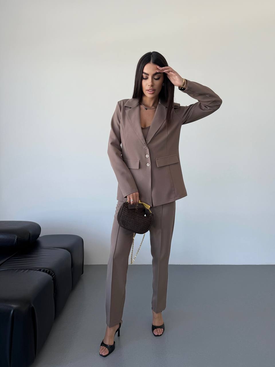 Woman in a brown suit standing in a minimalistic room with a black sofa.