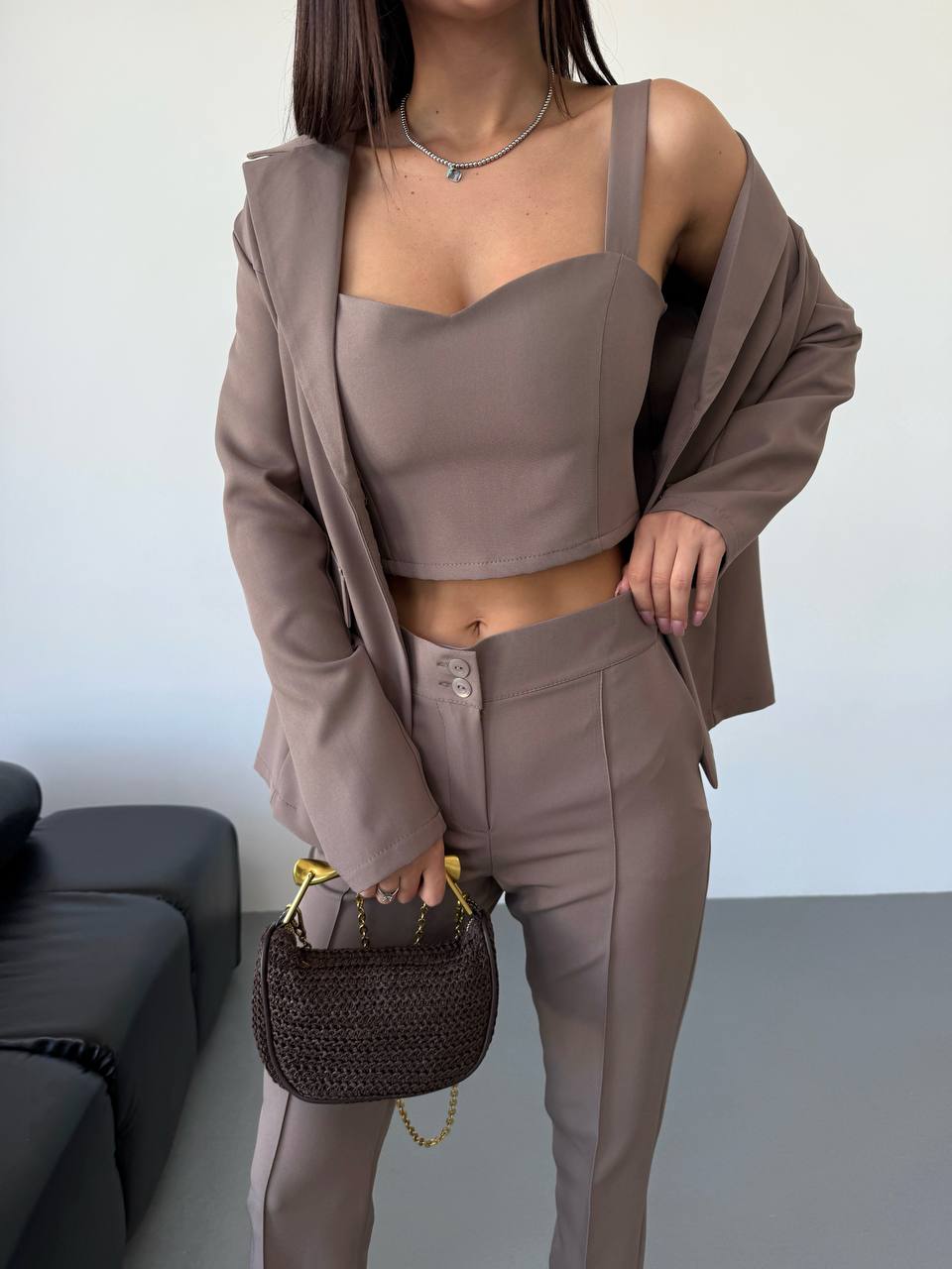 Woman wearing a brown outfit holding a handbag in an indoor setting