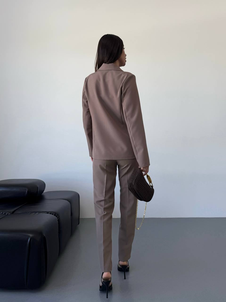 Person wearing a brown suit standing in a minimalistic room with a black sofa.