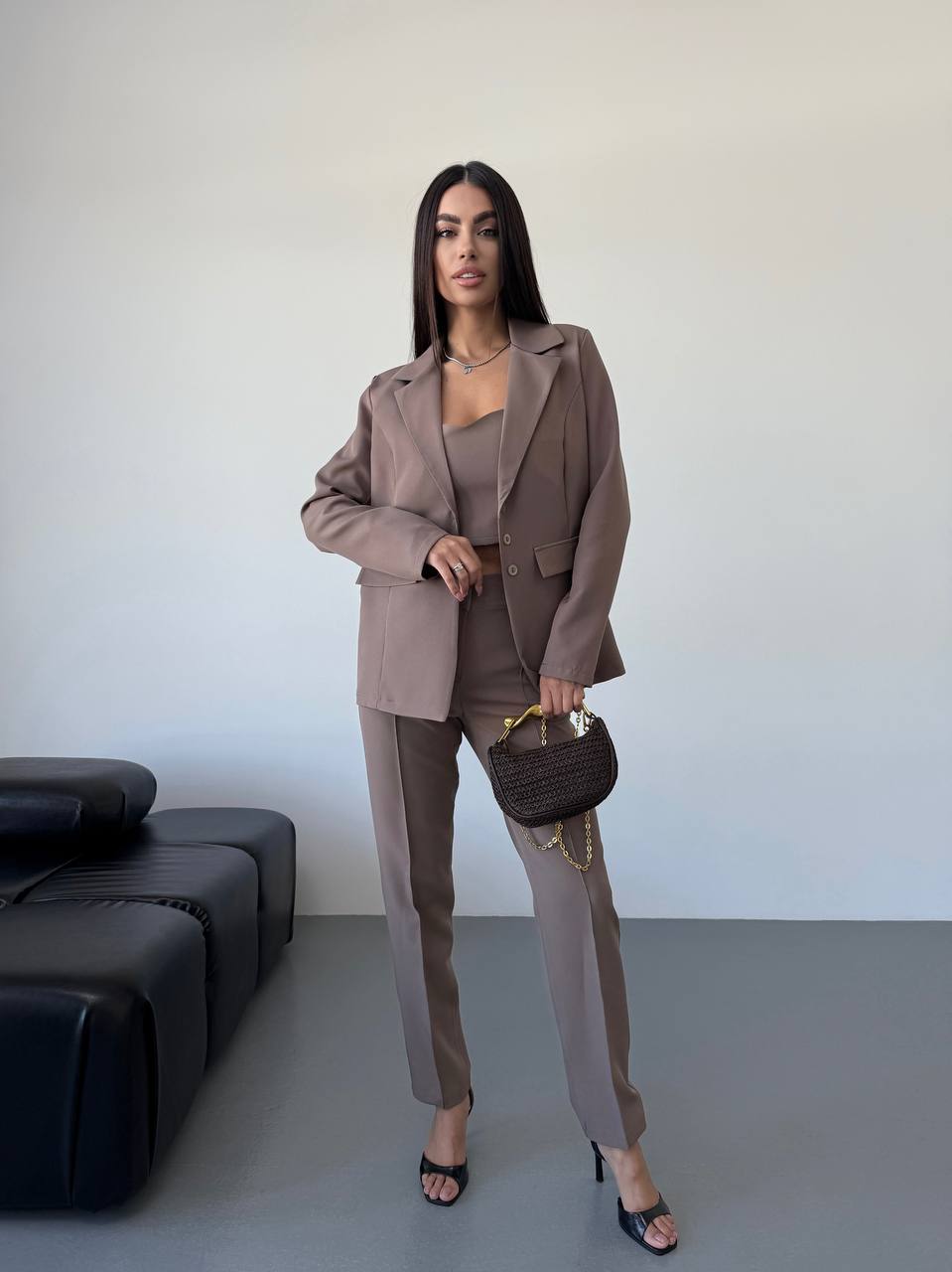 Woman in a brown suit standing in a minimalistic room with a black sofa.