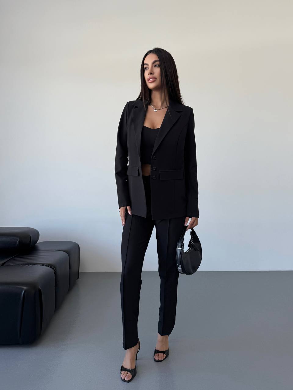 Woman in a black suit standing in a minimalistic room with a black couch.