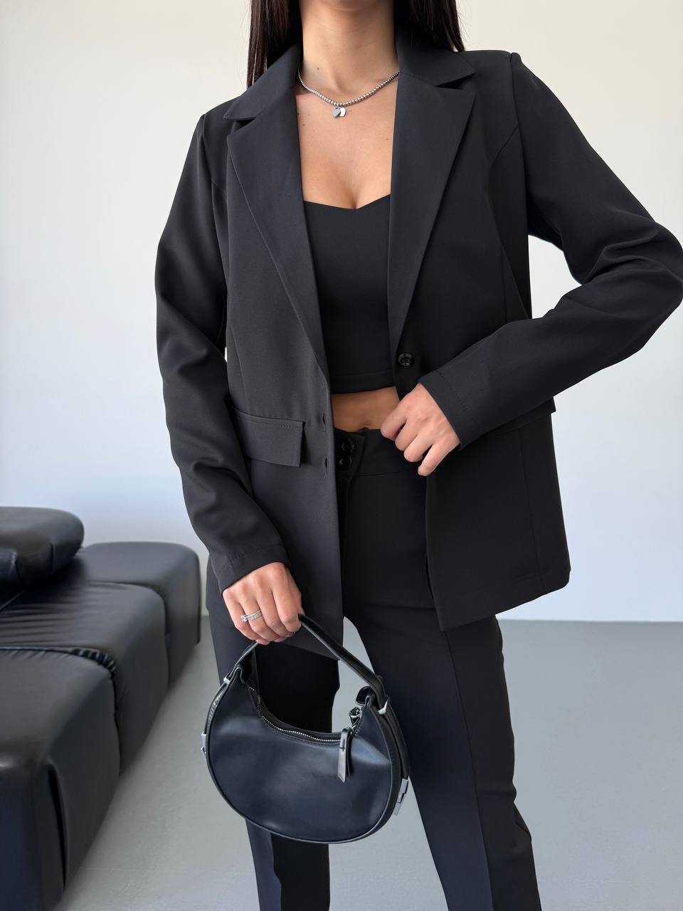 Person wearing a black blazer and holding a black handbag in an indoor setting.