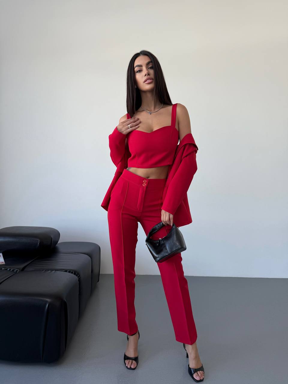 Woman in a red outfit standing in a minimalistic room with a black sofa.