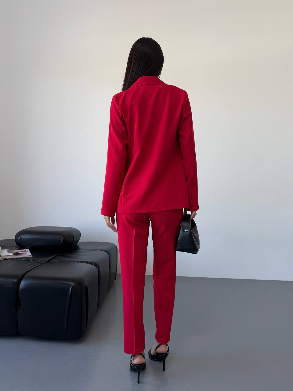 Person wearing a red suit standing in a minimalistic room with a black couch.