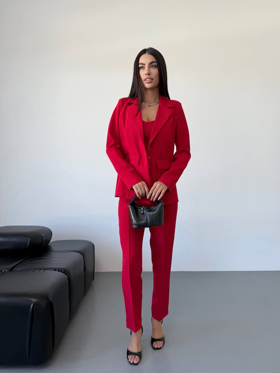 Woman in a red suit standing in a minimalistic room with a black couch.