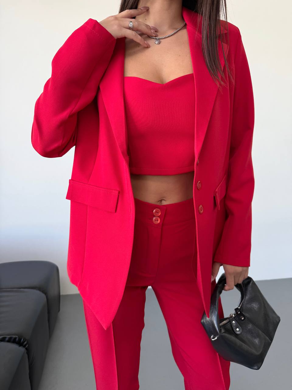 Person wearing a bright red outfit with a matching jacket, top, and pants, holding a black handbag.