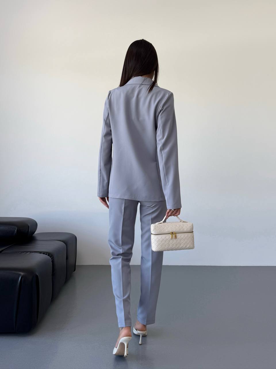 Person wearing a gray suit holding a beige handbag in an indoor setting.