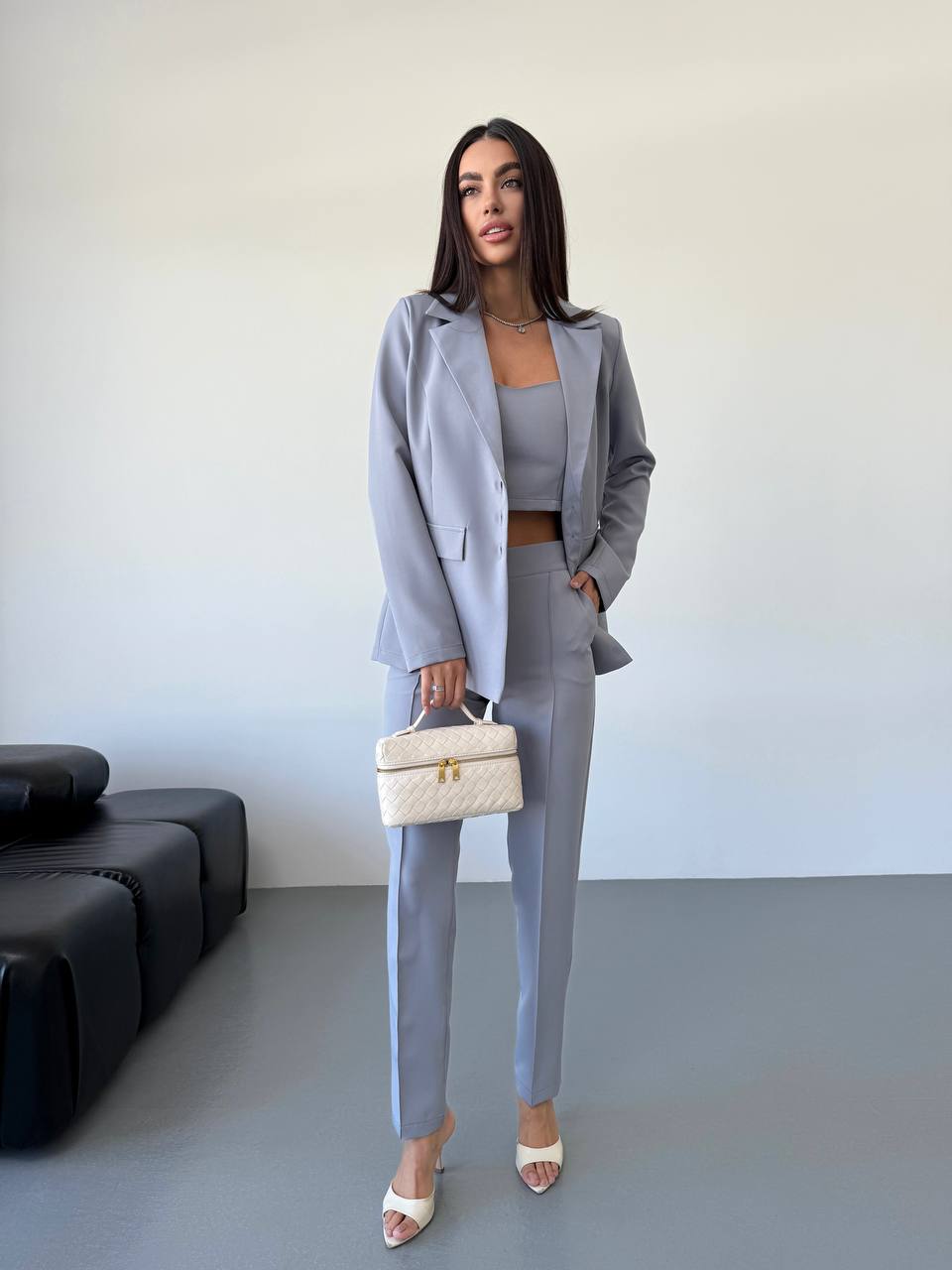 Woman in a gray suit standing in a minimalistic room with a black sofa and white wall.