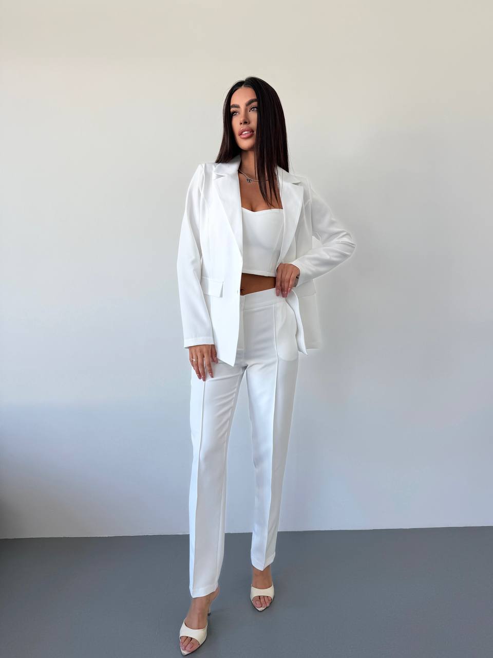 Woman wearing a white suit standing against a plain background