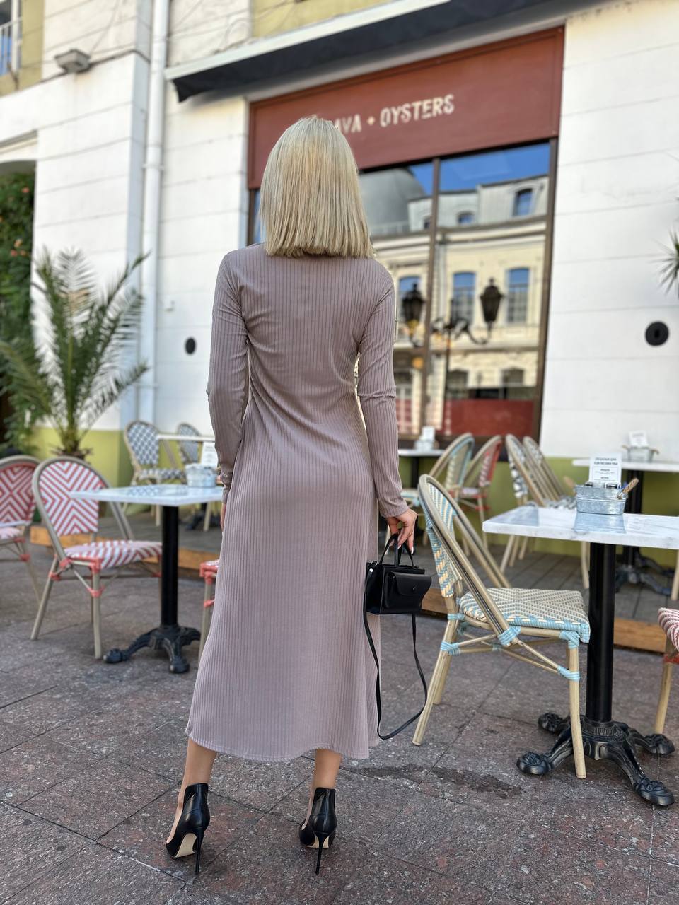 Woman in a long dress walking past a café with tables and chairs.