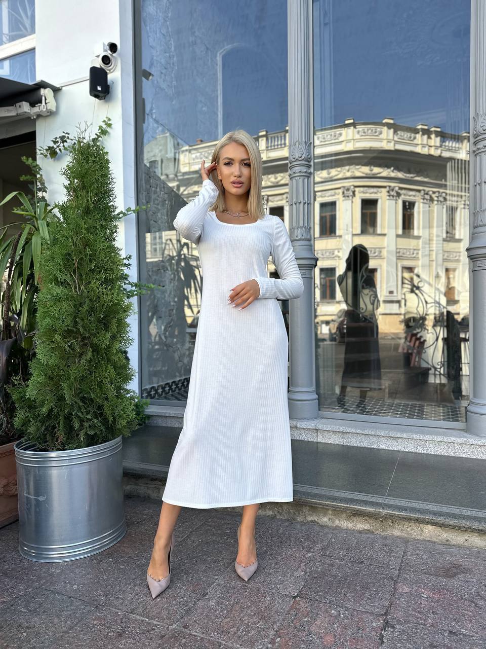 Woman in a white dress standing on a street with a building and plant in the background