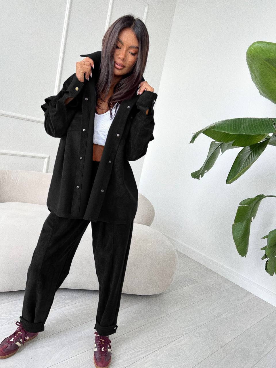 Woman in black outfit with white top in a minimalistic room with a plant.