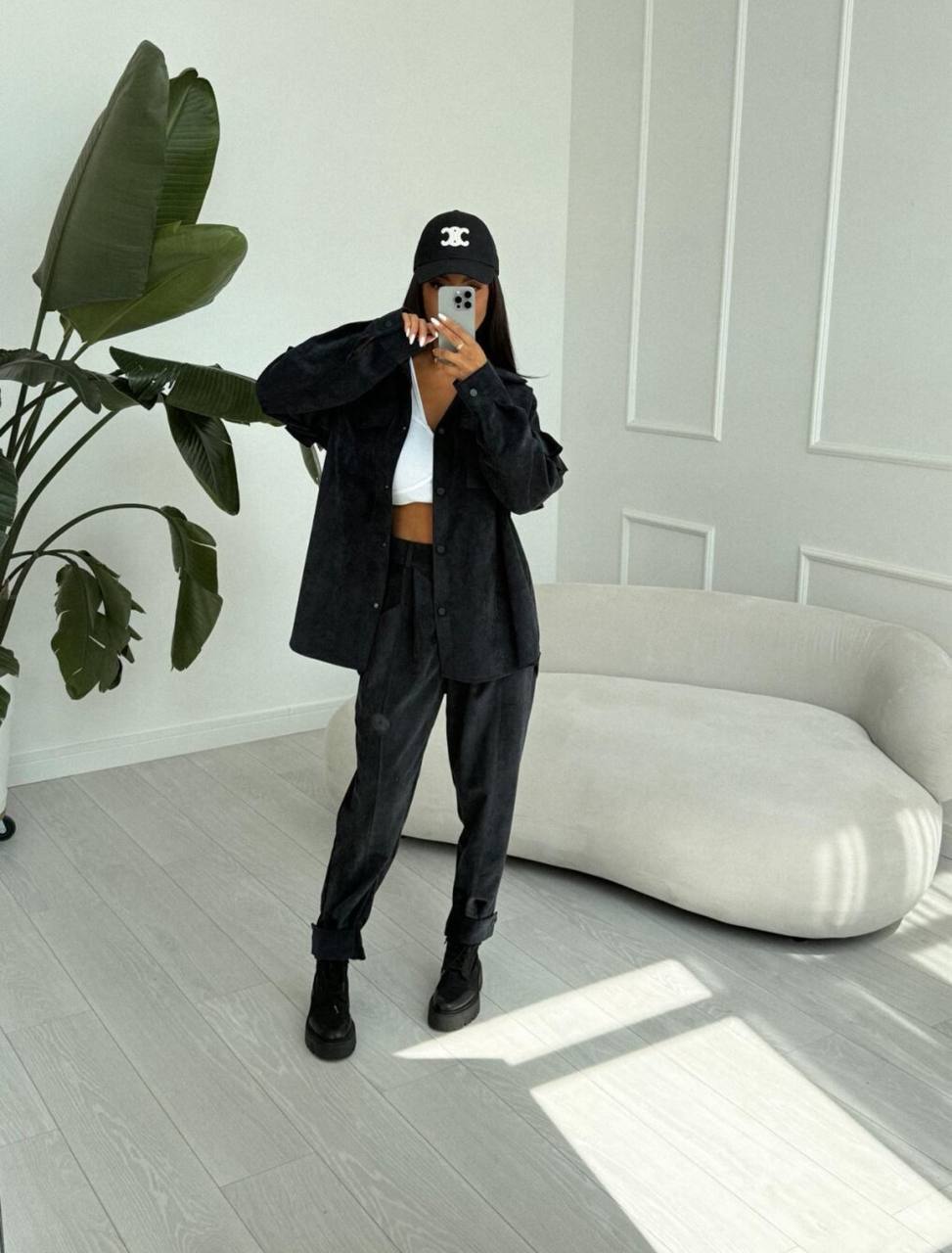 Person taking a mirror selfie in a modern living room wearing a black outfit.
