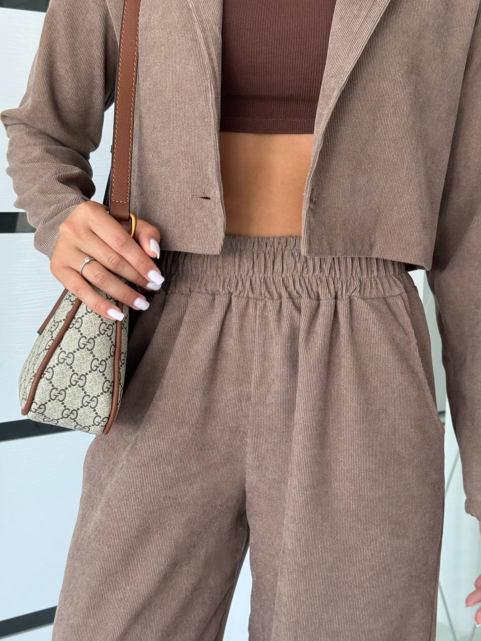 Person wearing a brown outfit with a matching jacket and pants, holding a Gucci handbag.