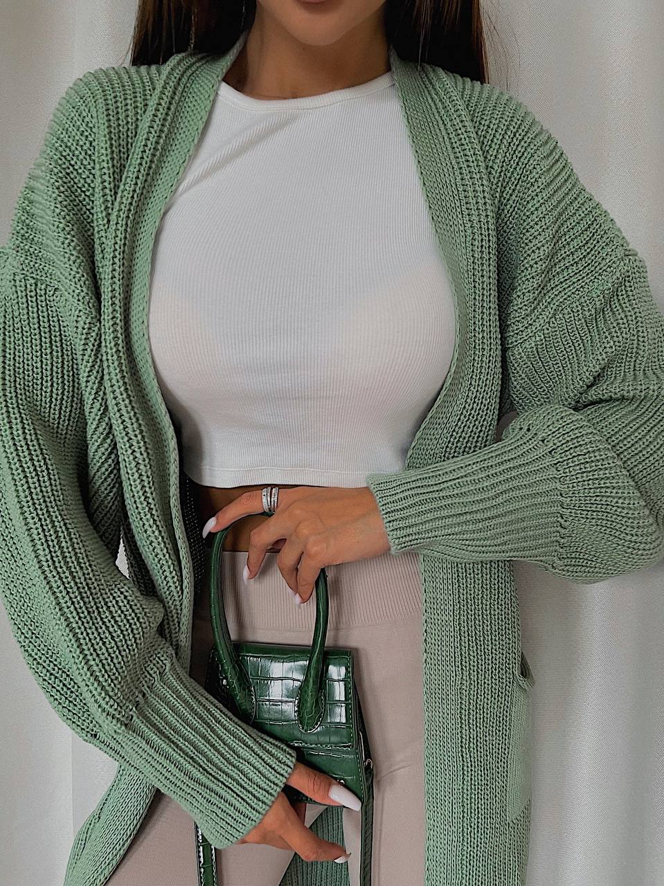 Person wearing a green knitted cardigan over a white top, holding a green handbag.
