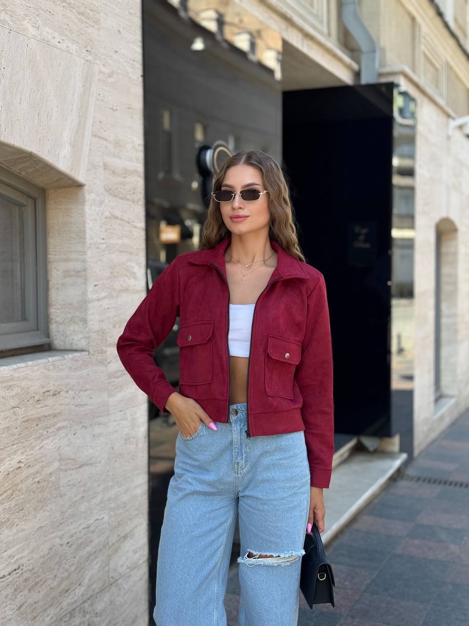 Woman wearing a red jacket, white top, and blue jeans standing on a street.