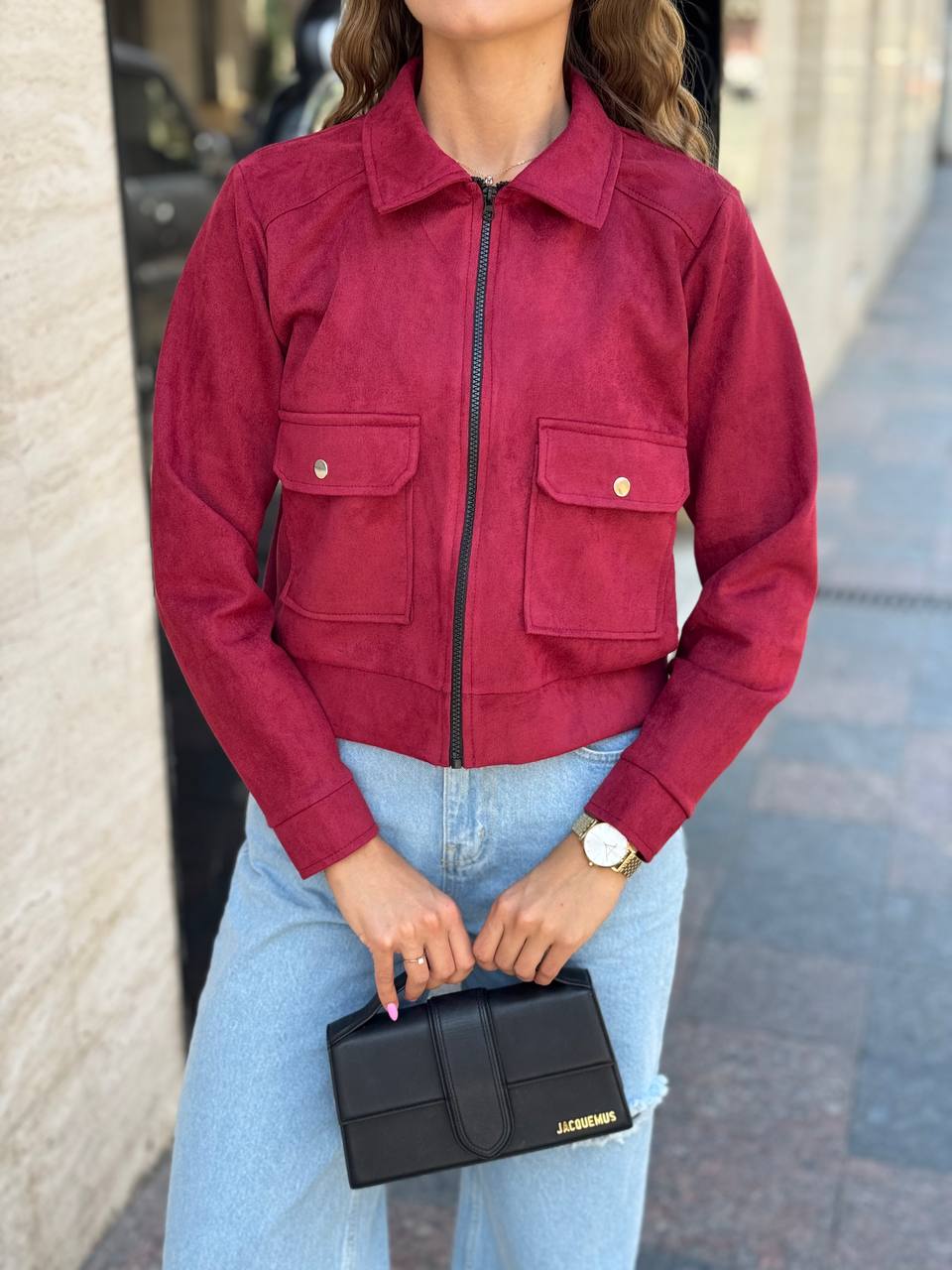 Person wearing a red jacket and light blue jeans, holding a black clutch.