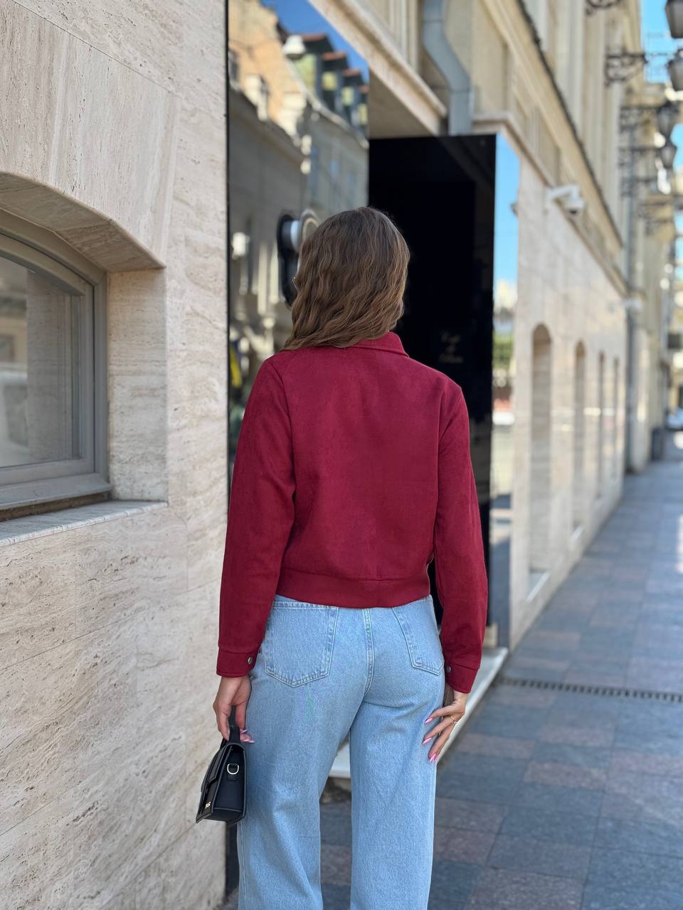 Person wearing a red jacket and light blue jeans standing on a street.