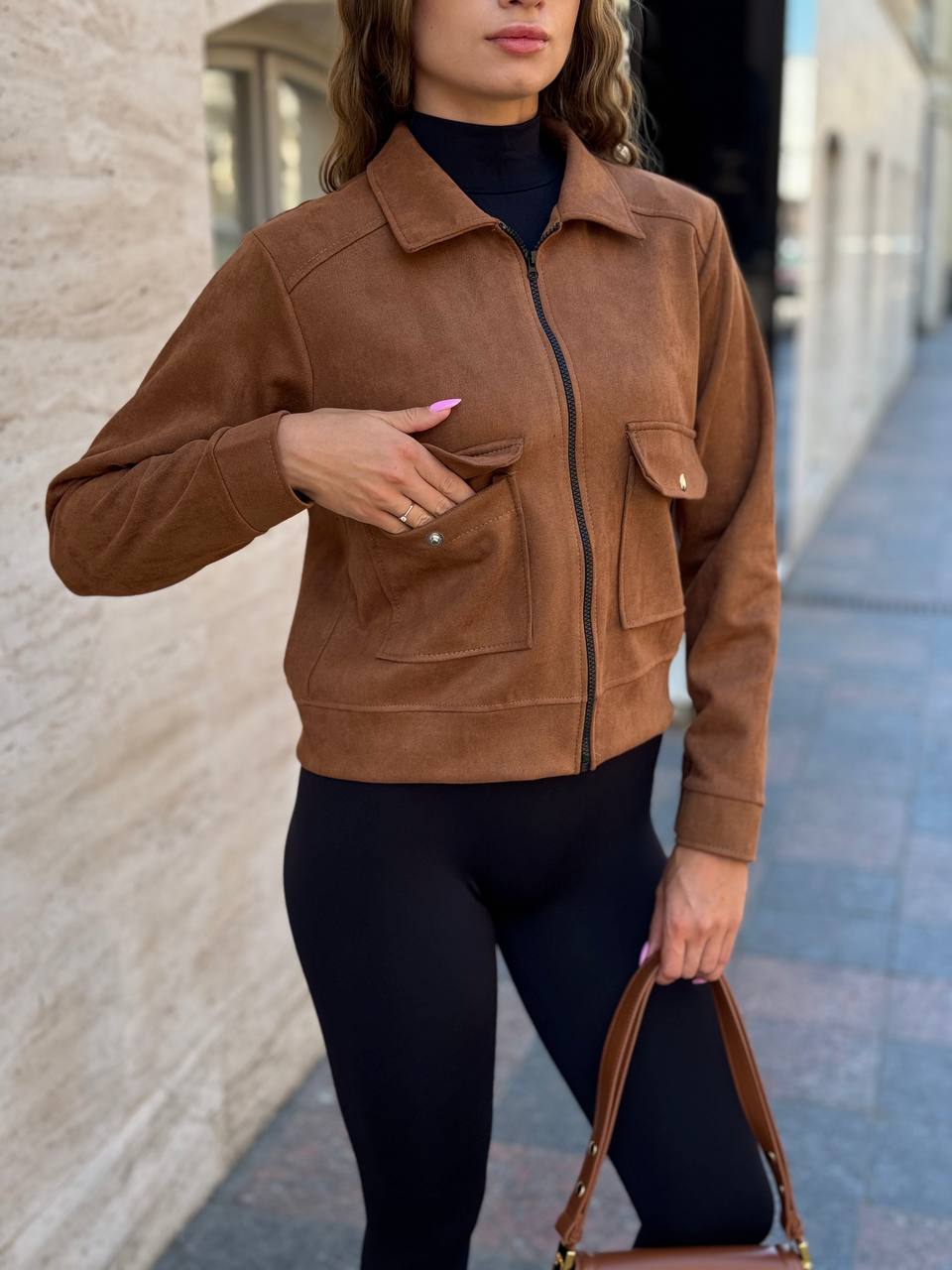 Woman wearing a brown suede jacket and black leggings outdoors.