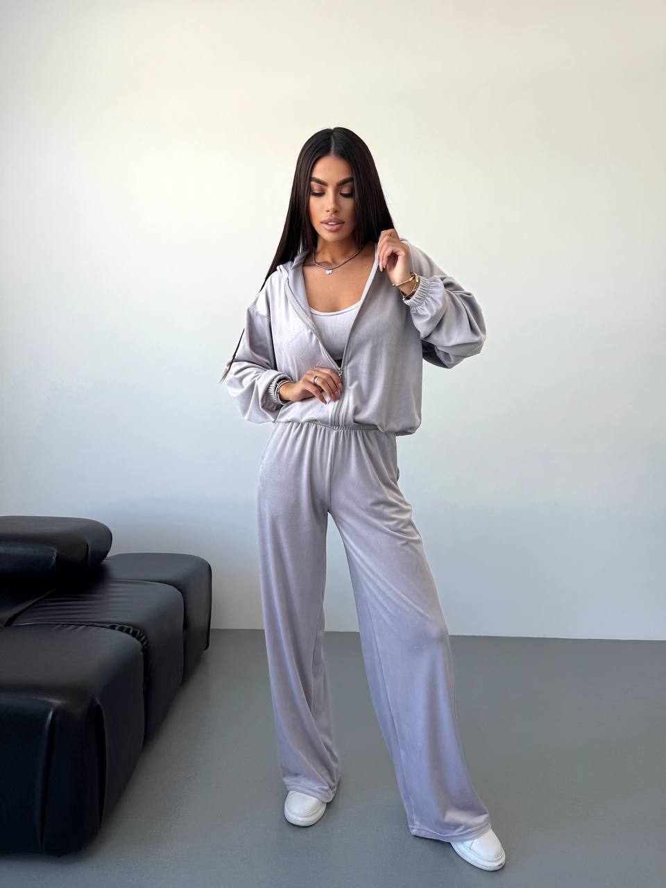 Woman wearing a light gray tracksuit in a minimalistic room.