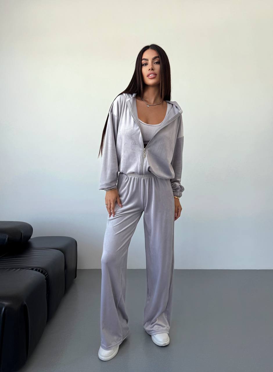 Woman wearing a gray tracksuit standing in a minimalistic room with a black sofa.