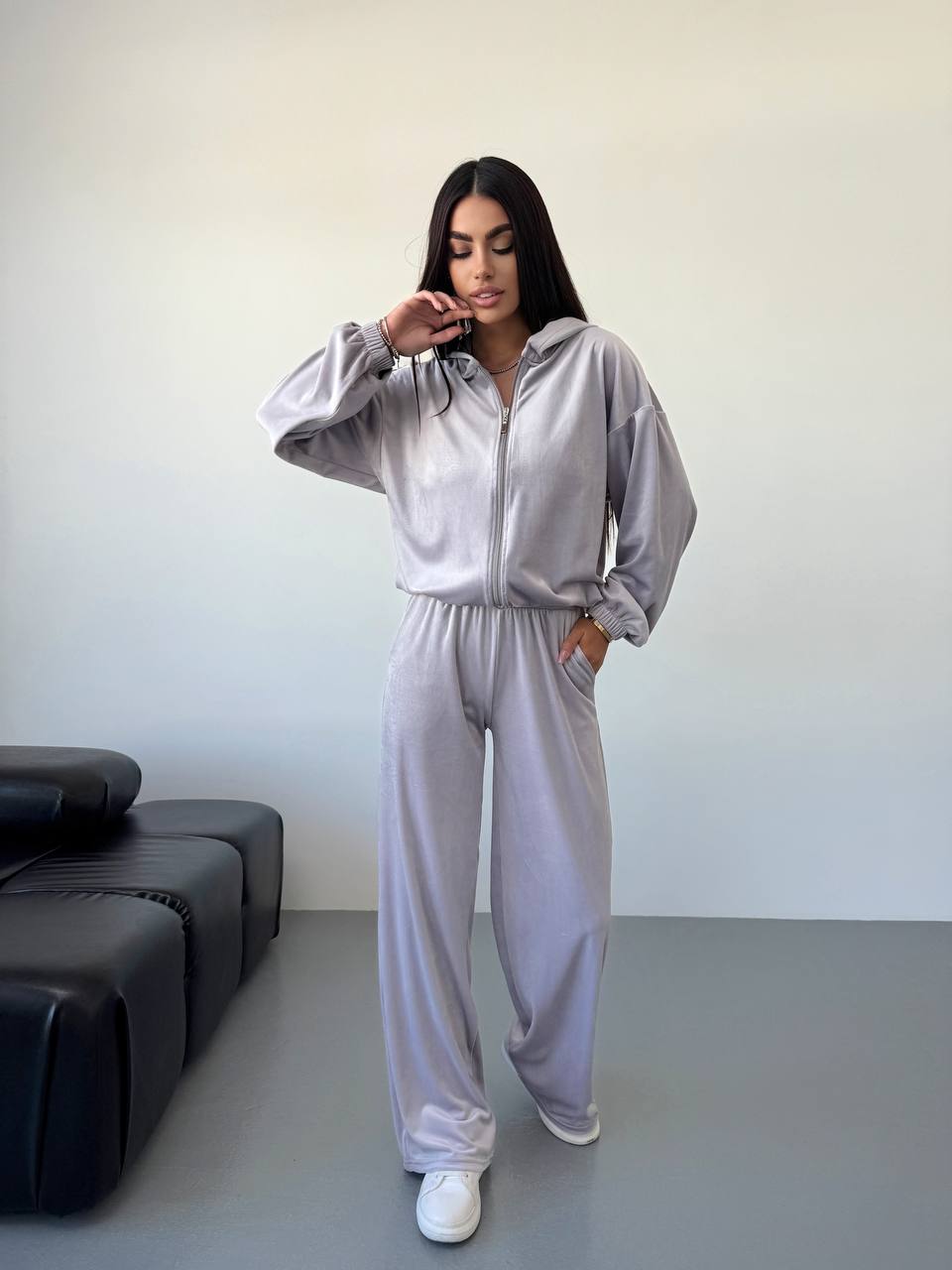 Person wearing a light gray tracksuit in a minimalistic room.