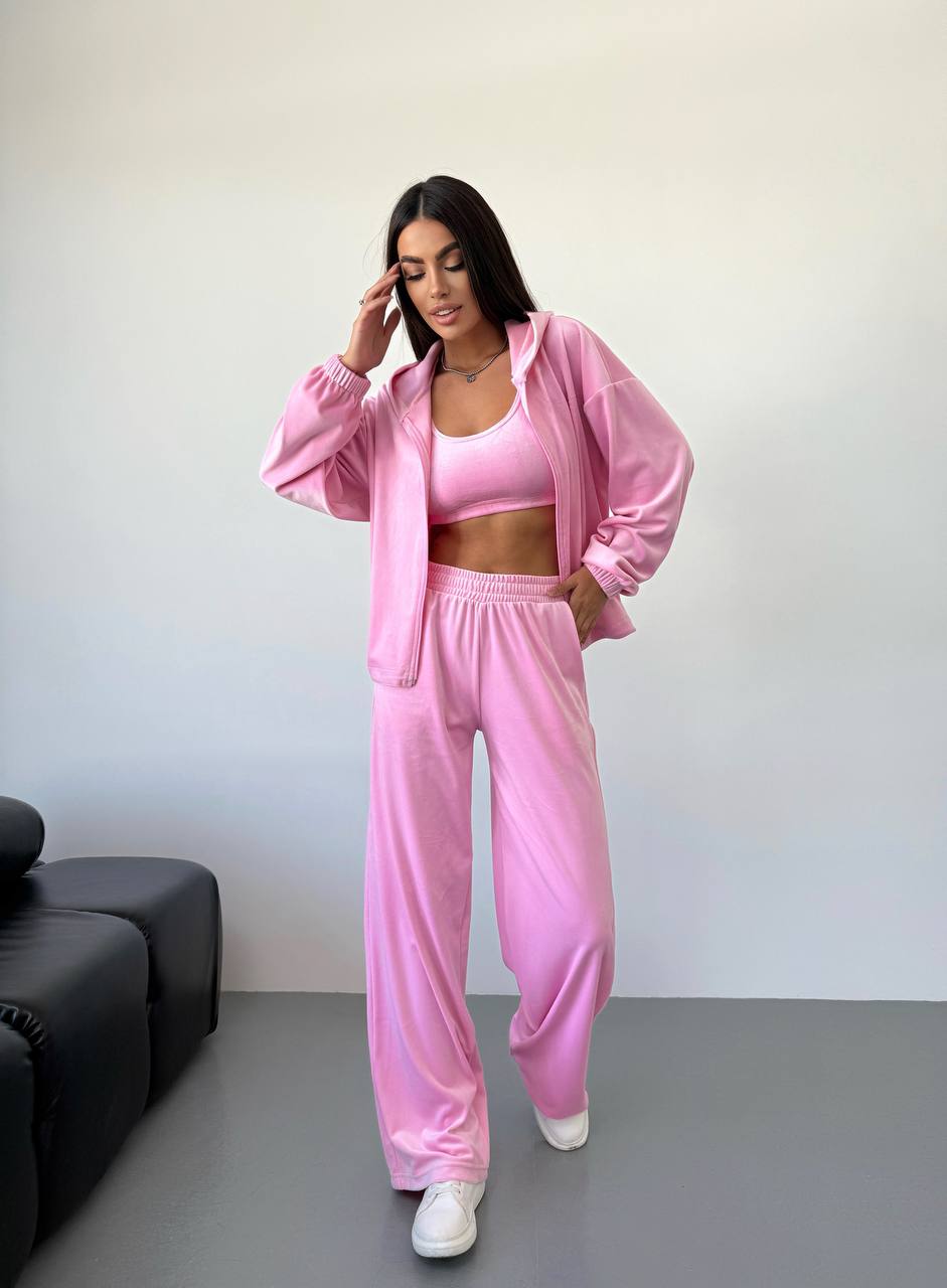 Woman wearing a pink tracksuit standing in a minimalistic room with a black sofa.