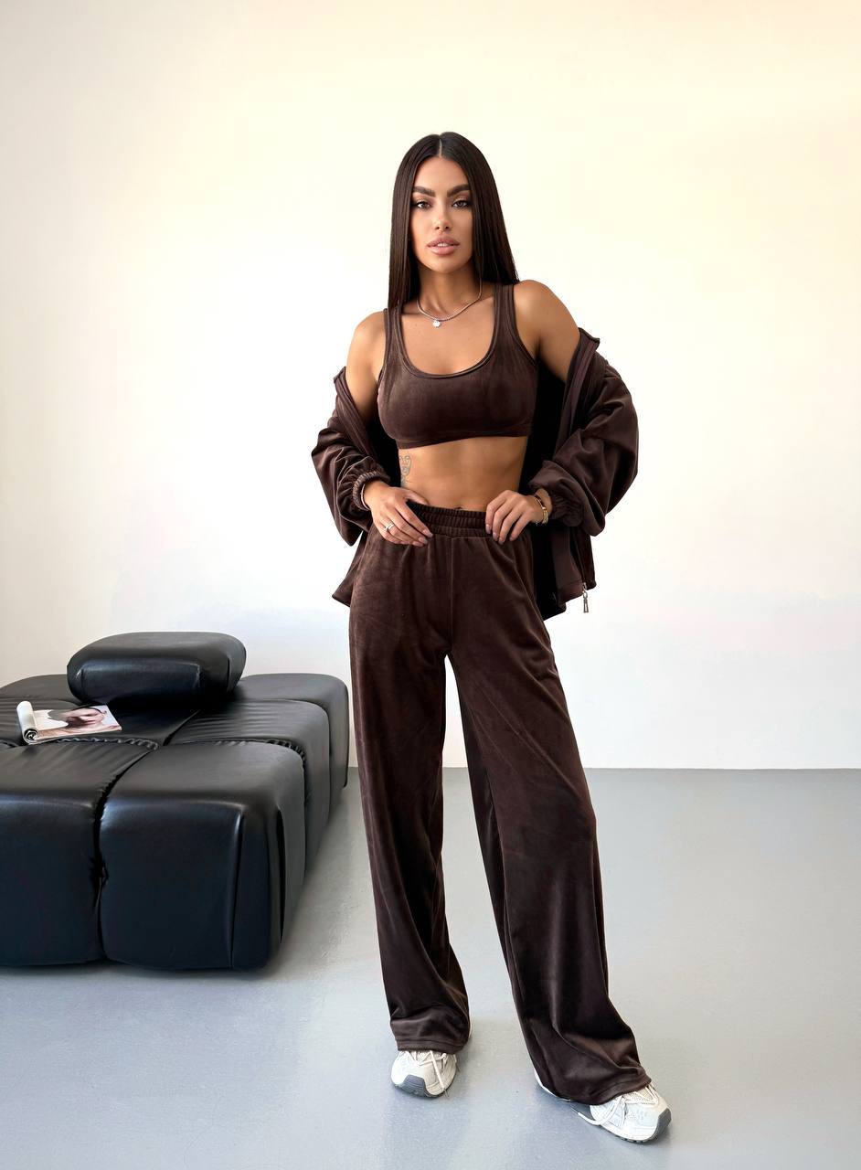 Woman in a brown outfit standing in a minimalistic room with a black sofa.