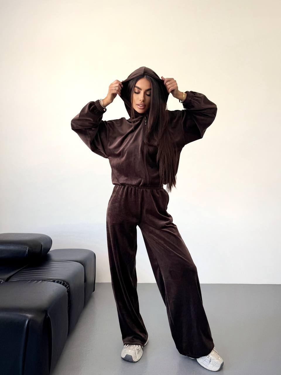 Person wearing a brown tracksuit standing in a minimalistic room with a black sofa.