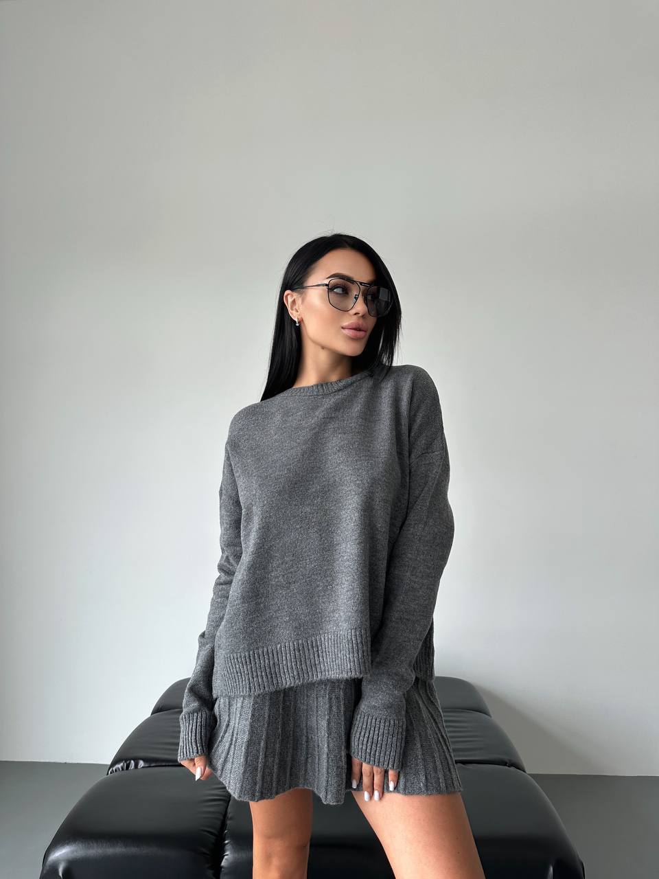 Woman wearing a gray sweater and skirt set against a plain background