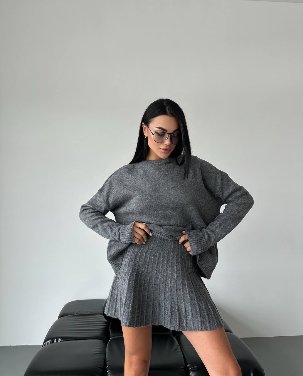 Woman wearing a gray sweater and skirt set against a plain background
