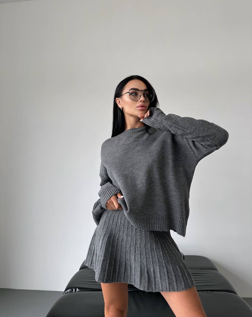 Woman wearing a gray sweater and skirt against a plain background