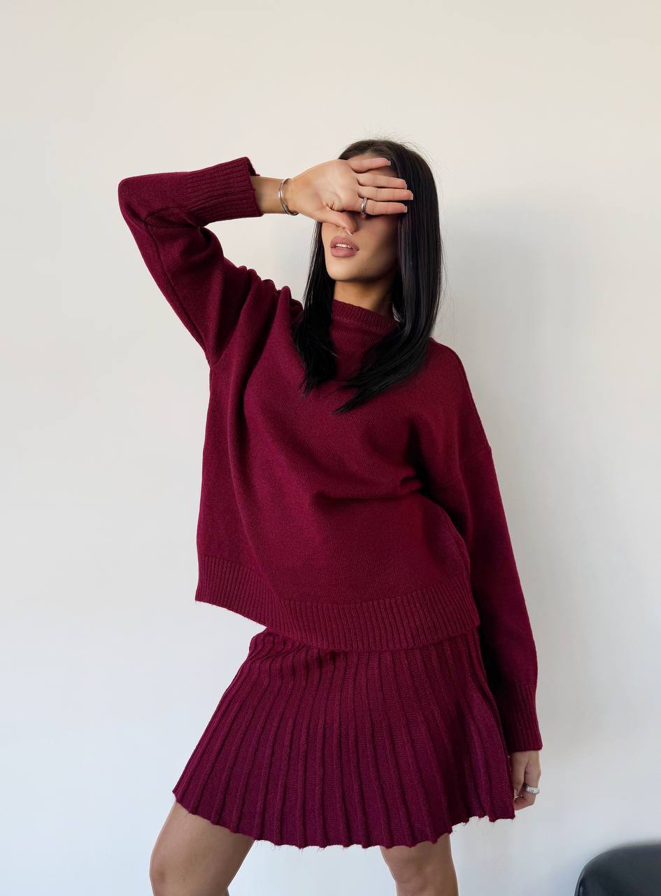Person wearing a maroon sweater and skirt set against a white background
