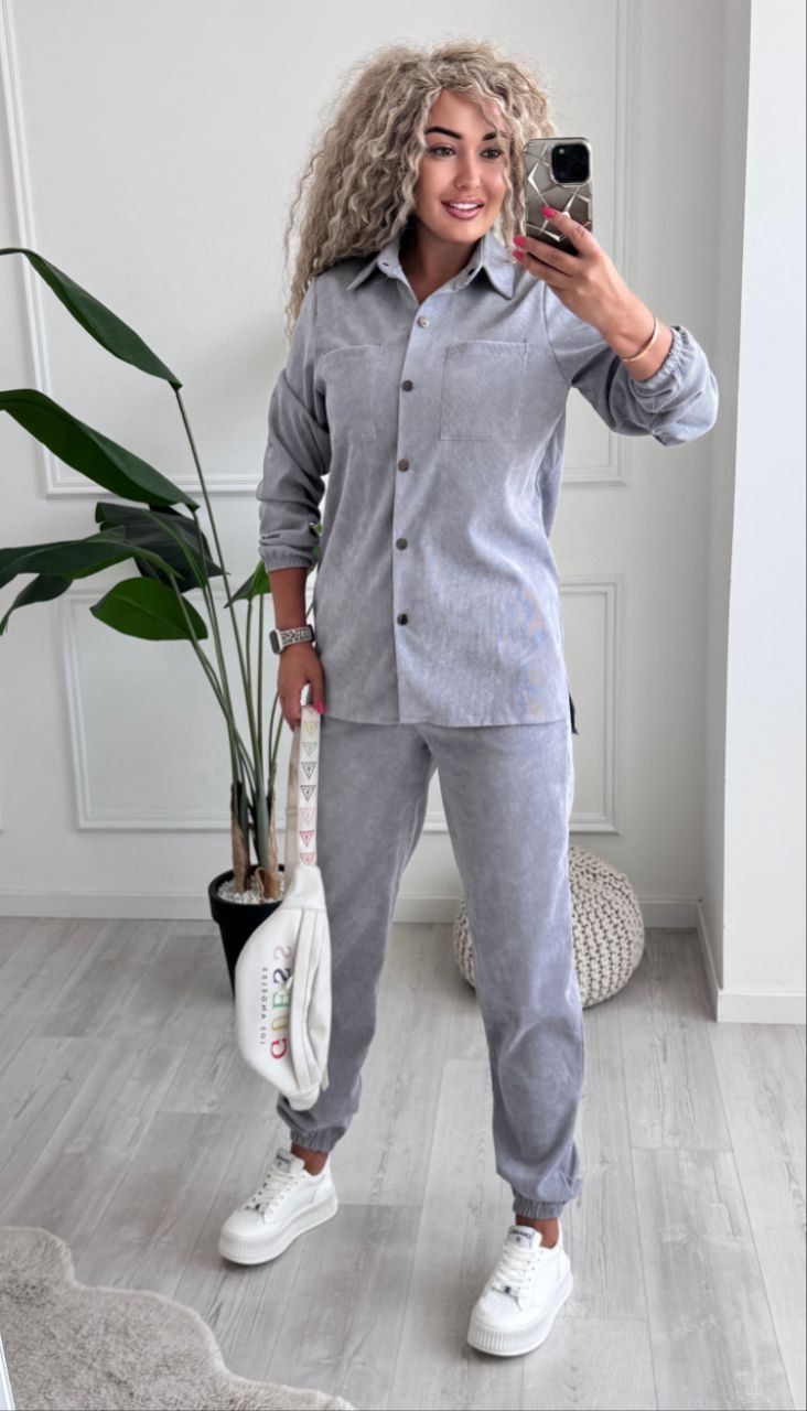 Person wearing a gray shirt and pants with white sneakers, standing indoors.