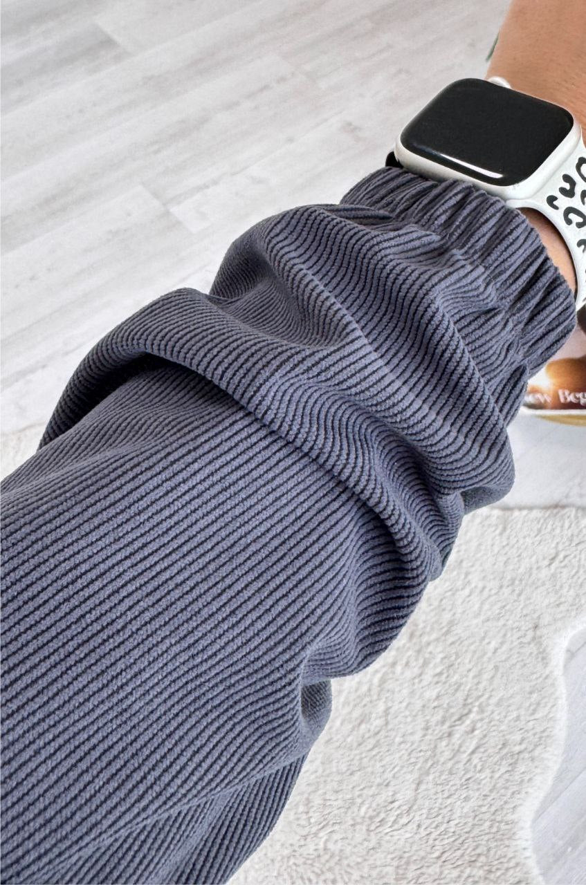 Person wearing a gray ribbed sweater with a blurred background