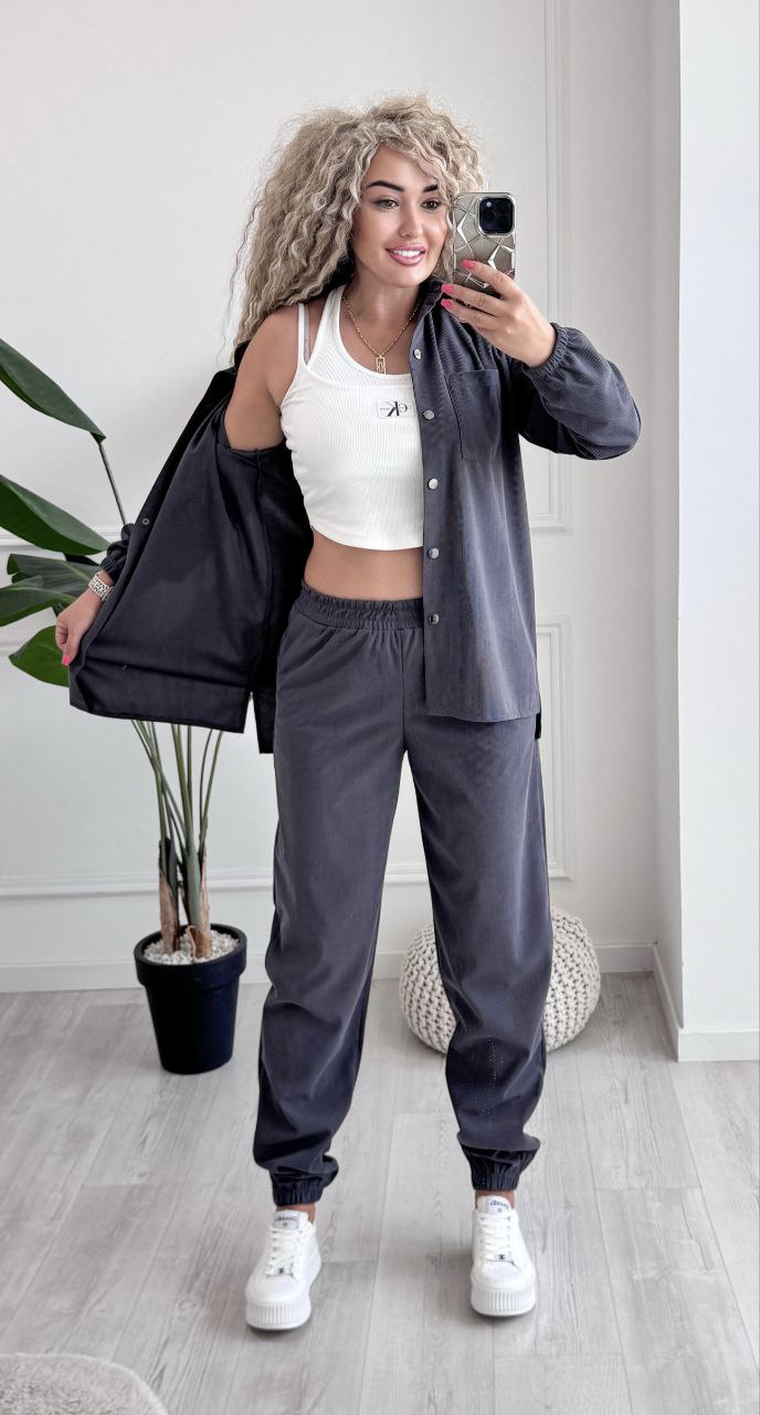 Woman taking a mirror selfie wearing a gray tracksuit and white sneakers in a minimalistic room.