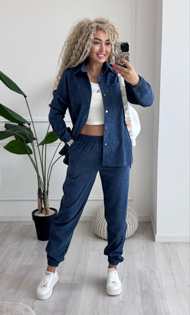 Woman taking a mirror selfie wearing a blue outfit with white sneakers in a room.