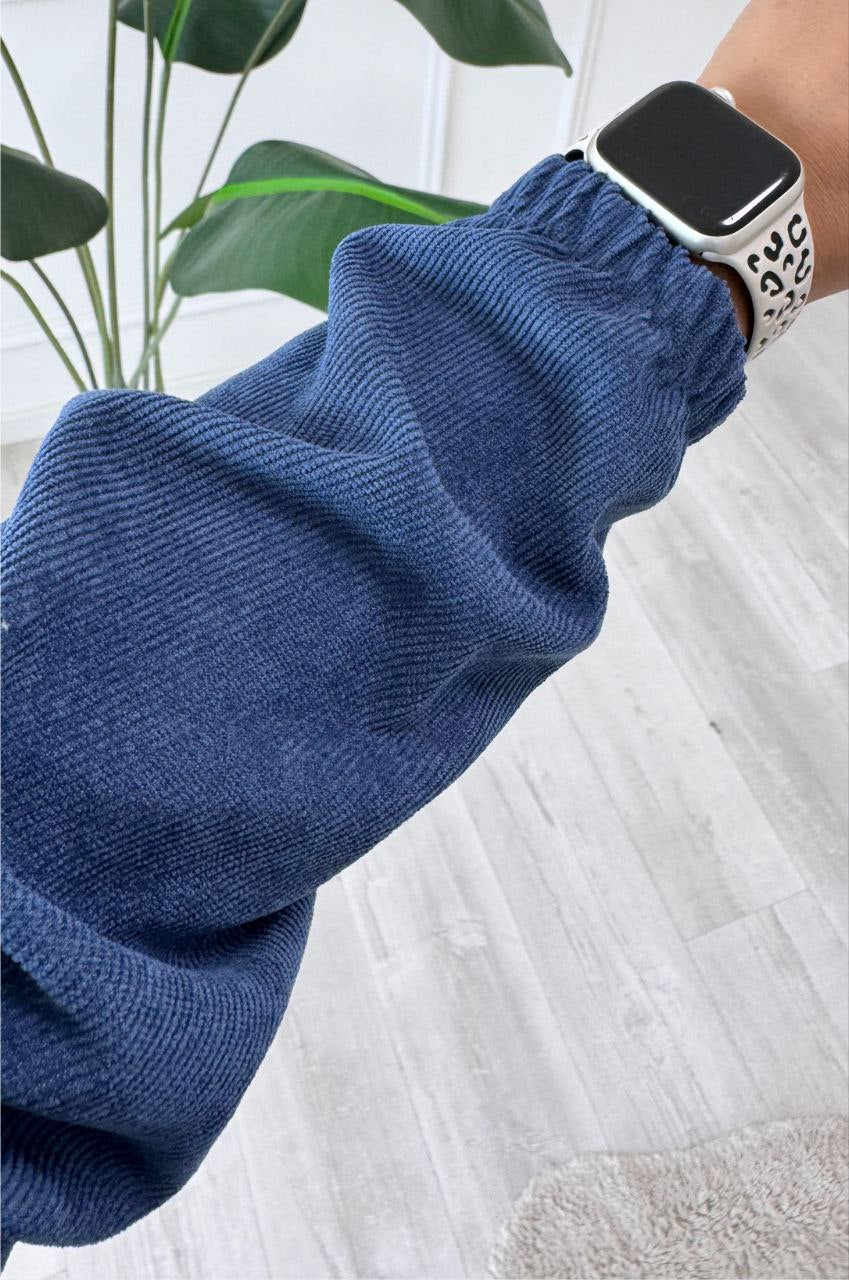 Blue knitted sleeve with a smartwatch on a light wooden floor.